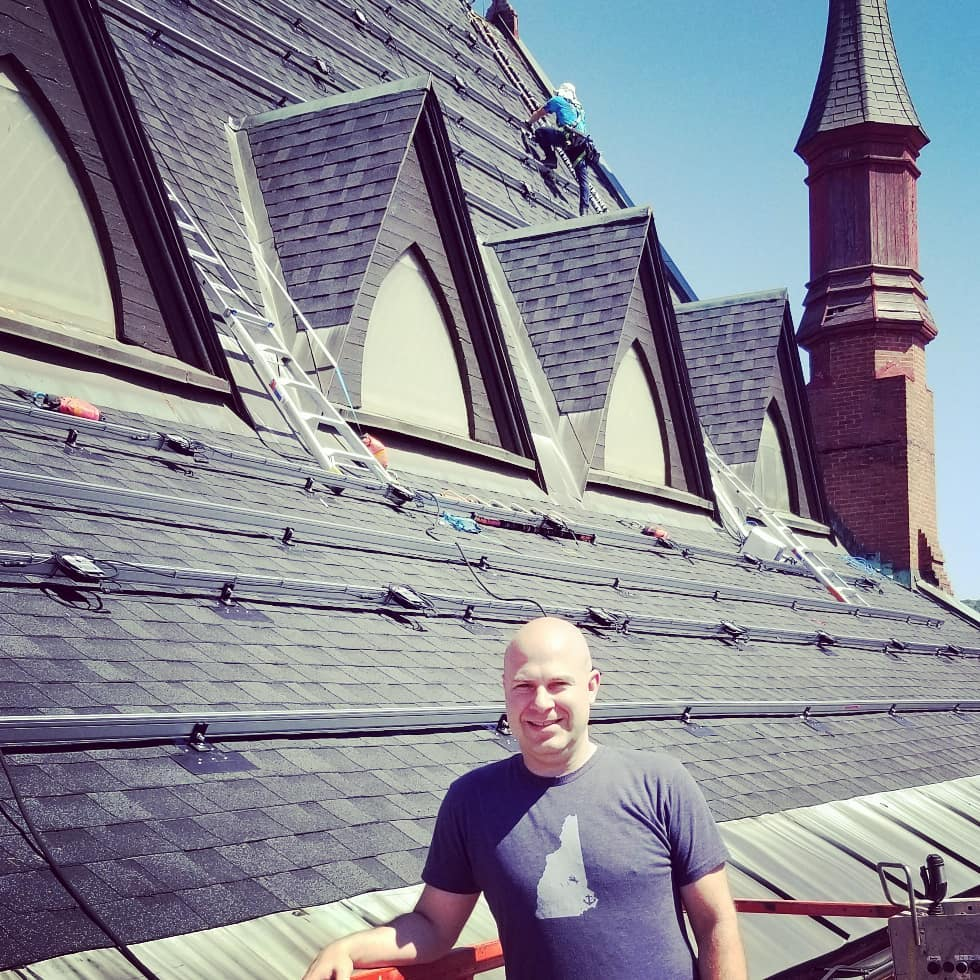 Zach Luse in front of an in progress solar installation on the roof of 34 Court Street, Keene, NH.